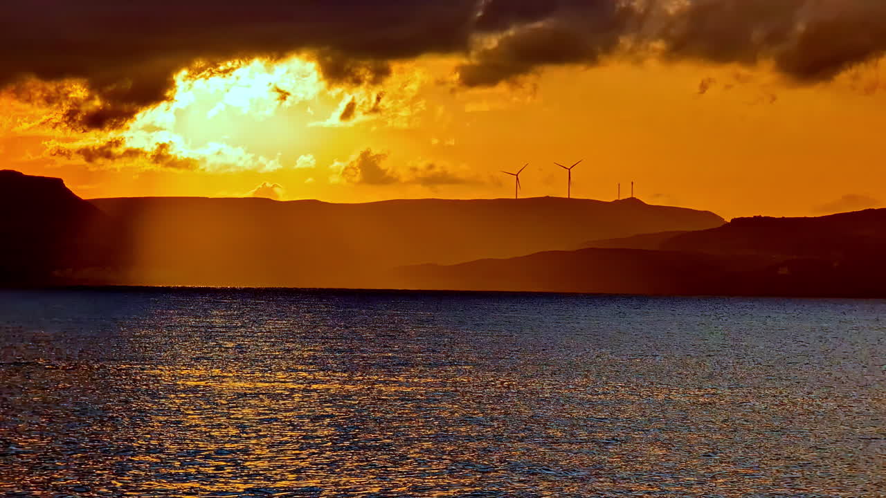 Mountainous coastline of Crete with wind power turbines, dramatic sunset in Greece