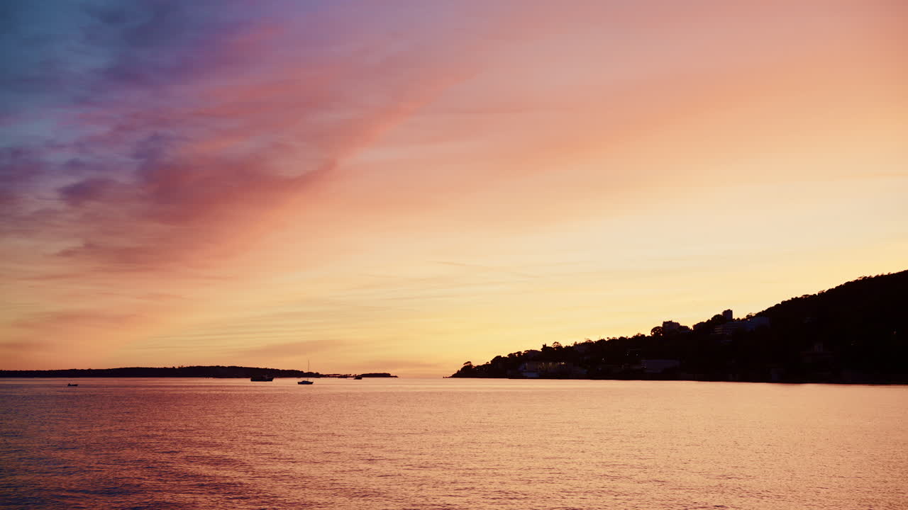 Beautiful sunset sky in warm shades of orange, pink, and purple above a calm coastline in the French Riviera