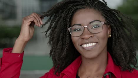 Mujer-Afroamericana-Mirando-A-La-Cámara,-Sonriendo,-Corrigiendo-El-Cabello