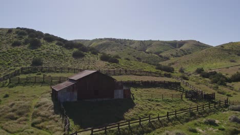 Forward-Aerial-Shot-of-Abandoned-Barn-in-the-Green-Hills-of-Carrizo-Plain-in-California