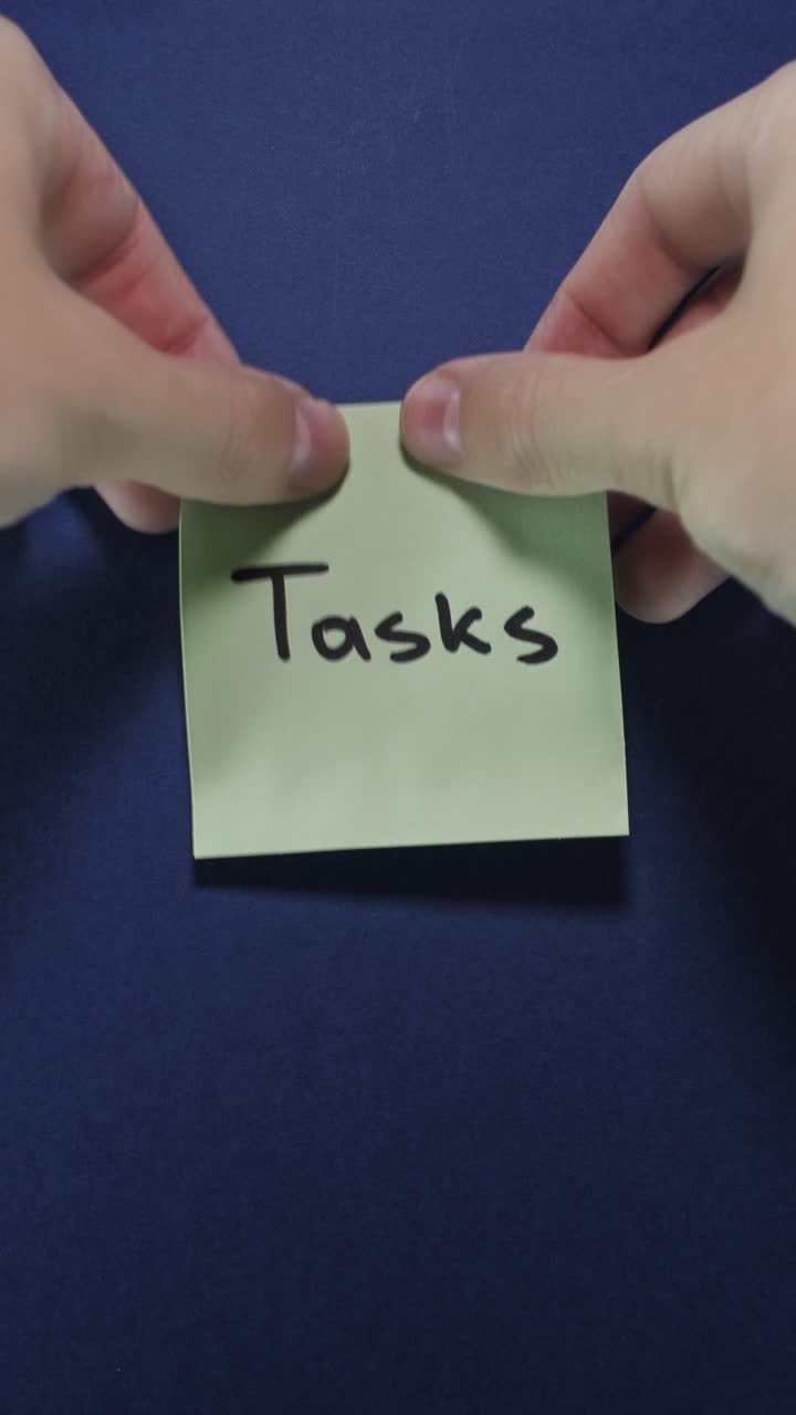 Portrait shot of a light green sticky note reading "Tasks" on a dark blue background