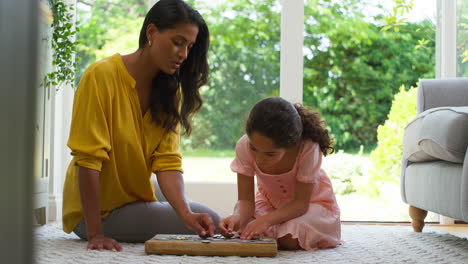 mother and daughter at home sitting on floor in lounge doing jigsaw puzzle together