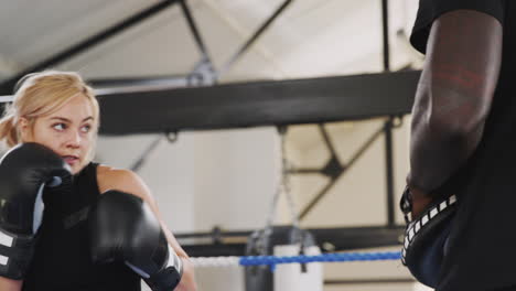 Male-Boxing-Coach-With-Female-Boxer-In-Gym-Using-Training-Gloves-Sparring-In-Ring