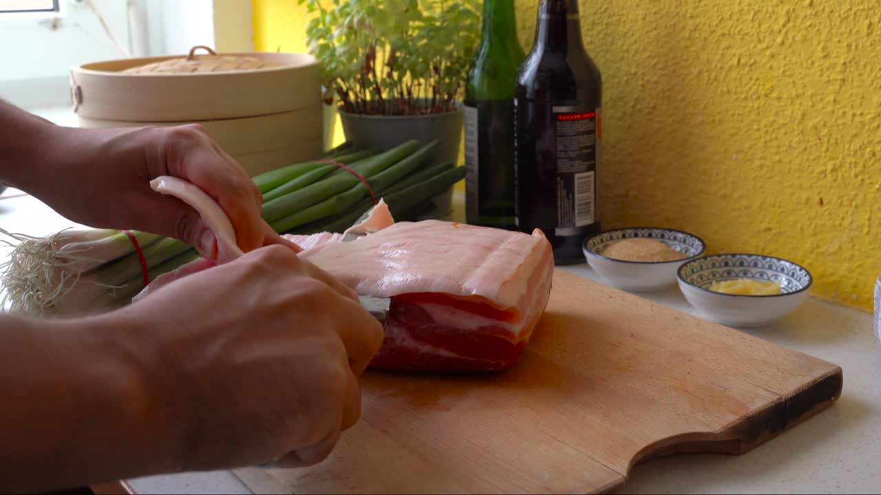 Male hands cutting off skin from pork belly piece in home kitchen setting