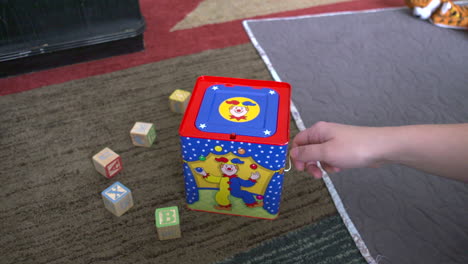 a woman's hand winding a jack-in-the-box toy until it pops up