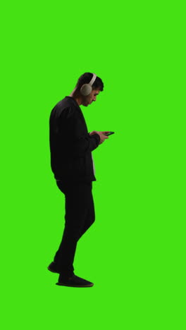 Vertical-Video-Full-Length-Shot-Of-Man-Wearing-Wireless-Headphones-Streaming-Music-From-Mobile-Phone-Against-Green-Screen-3