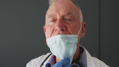 Portrait-of-caucasian-senior-male-doctor-lowering-his-face-mask-and-smiling