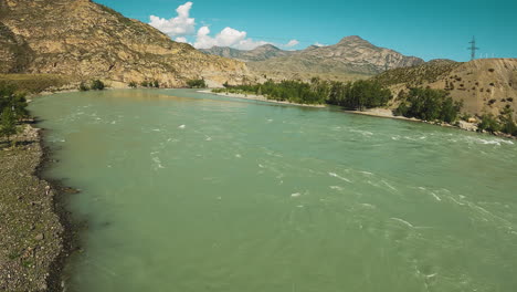 large mountain river runs between hills fpv. rough waterway stream with tourist camp on bank on nice sunny day. stunning landscape of wilderness