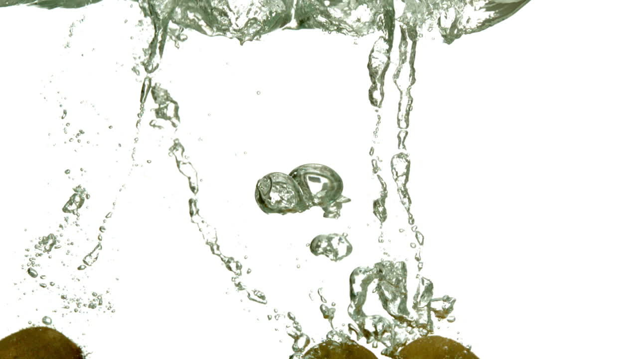 Three kiwi fruits plunging into water on white background