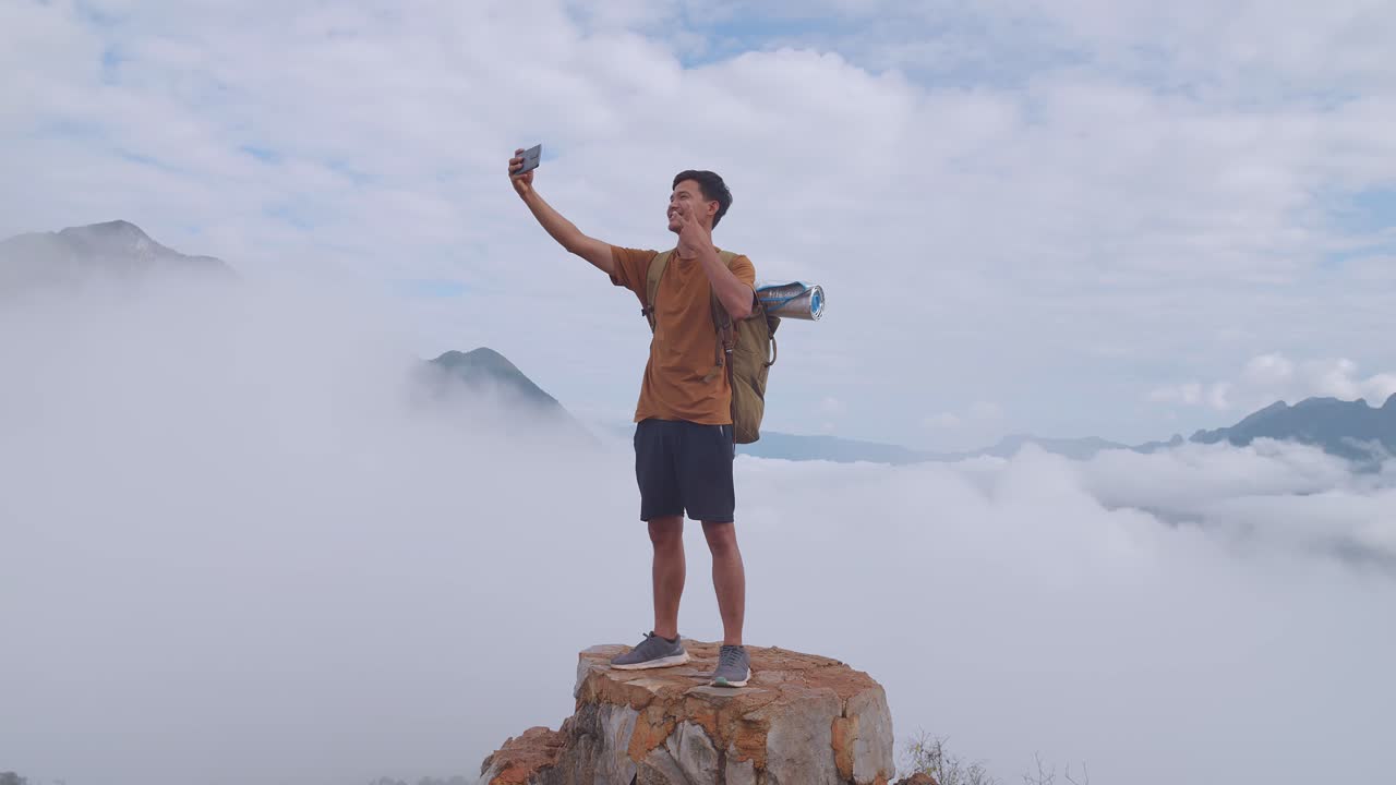 스마트워치를 이용해 산 위에 서서 안개가 가득한 산의 전망을 가지고 셀피 사진을 찍는 아시아의 하이커 남성