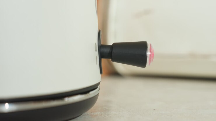 Close up of hand placing electric kettle on base as red indicator light blinks to show power is on, capturing subtle kitchen details and motion in warm natural light setting