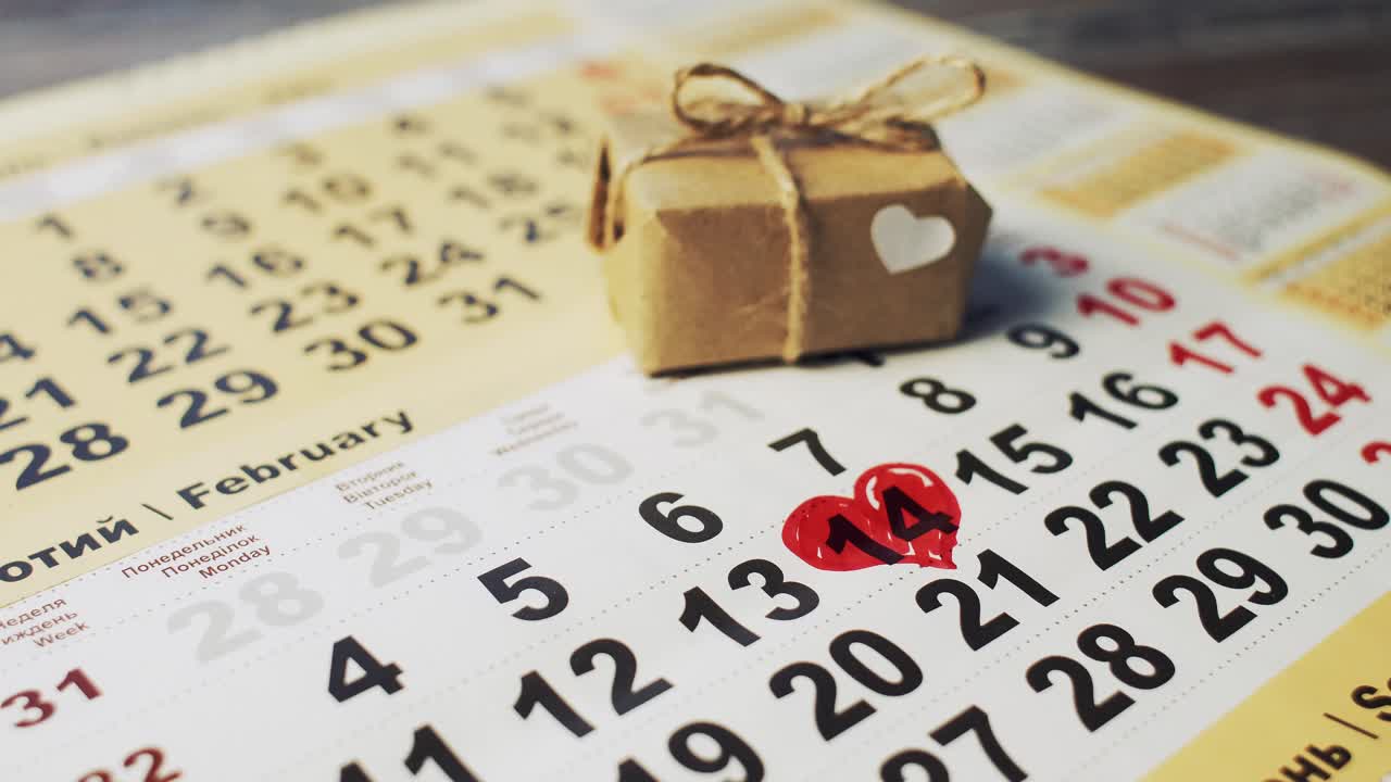 Male hand with red marker paint a heart shape in the calendar february 14th near gift. Valentine's day