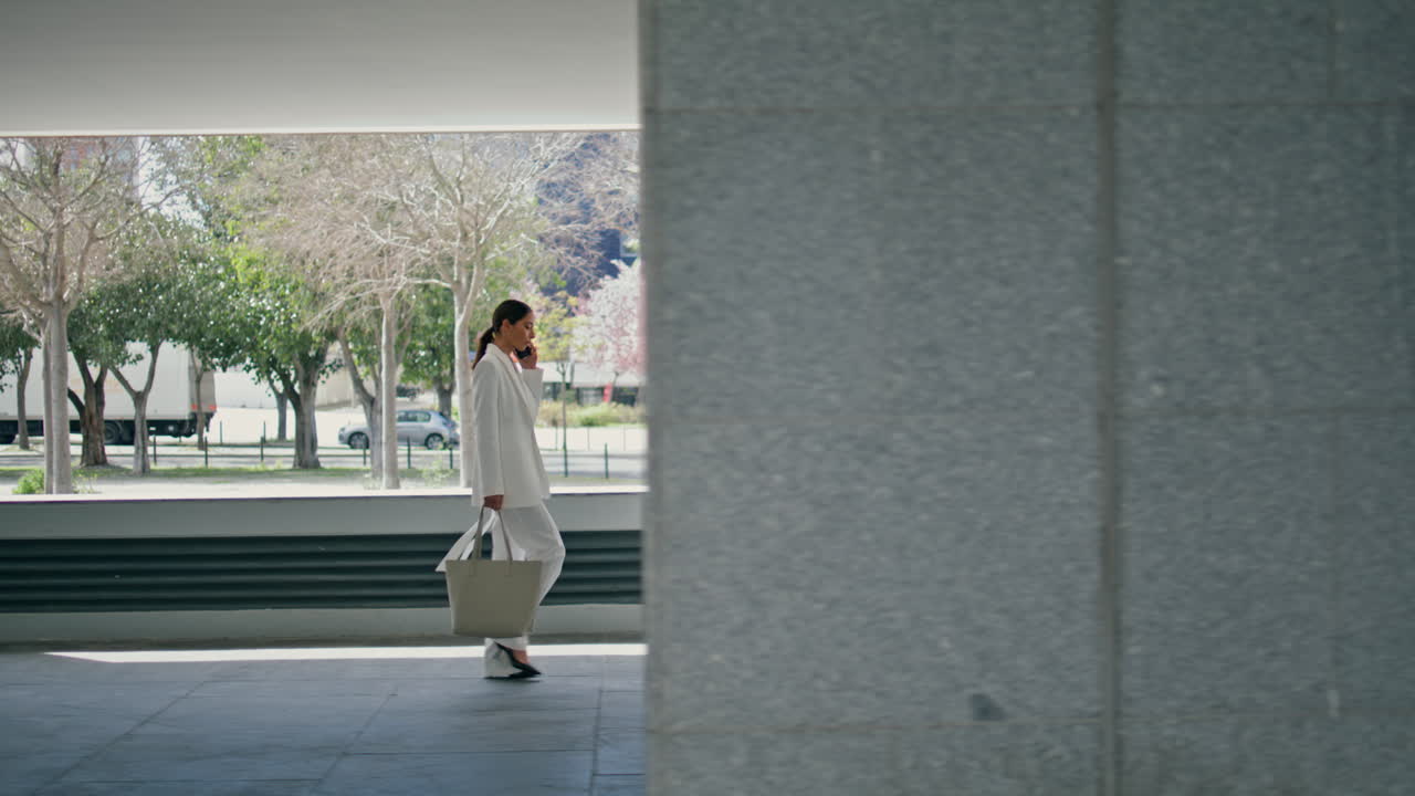 mujer adinerada caminando edificio de oficinas moderno hablando teléfono inteligente. señora llamando
