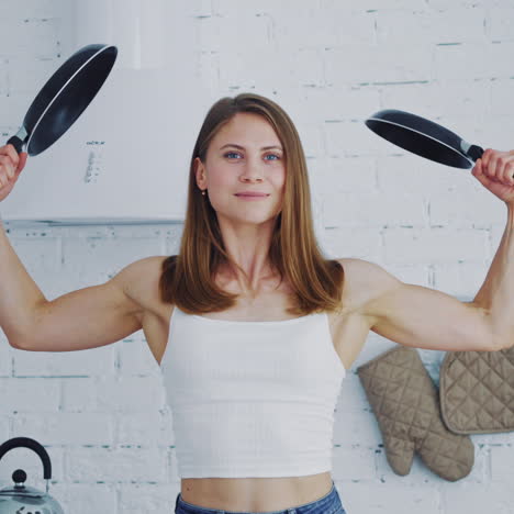pretty female with frying pans at home. muscular young woman holding two empty frying pans. healthy housewife posing to camera.