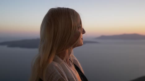 mujer rubia sonriendo y viendo la puesta de sol sobre la isla santorini grecia