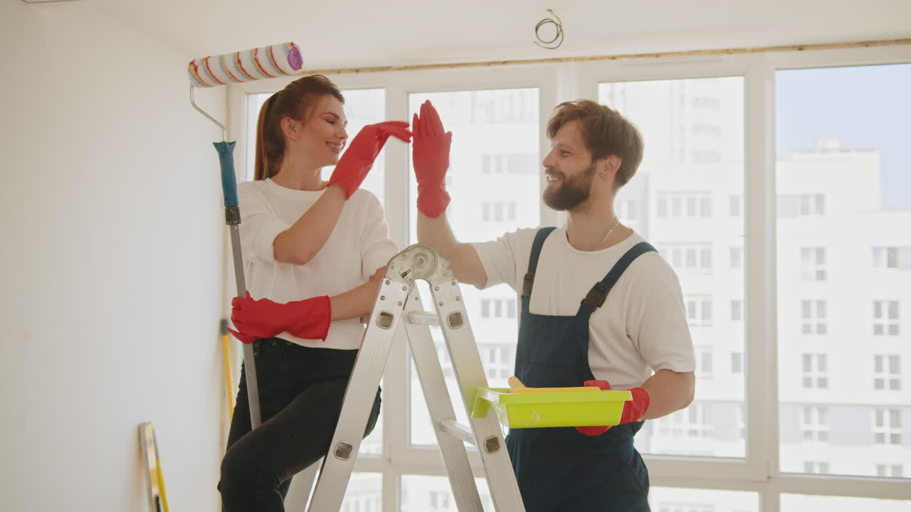 счастливая пара даёт пять после того, как закончила красить комнату.