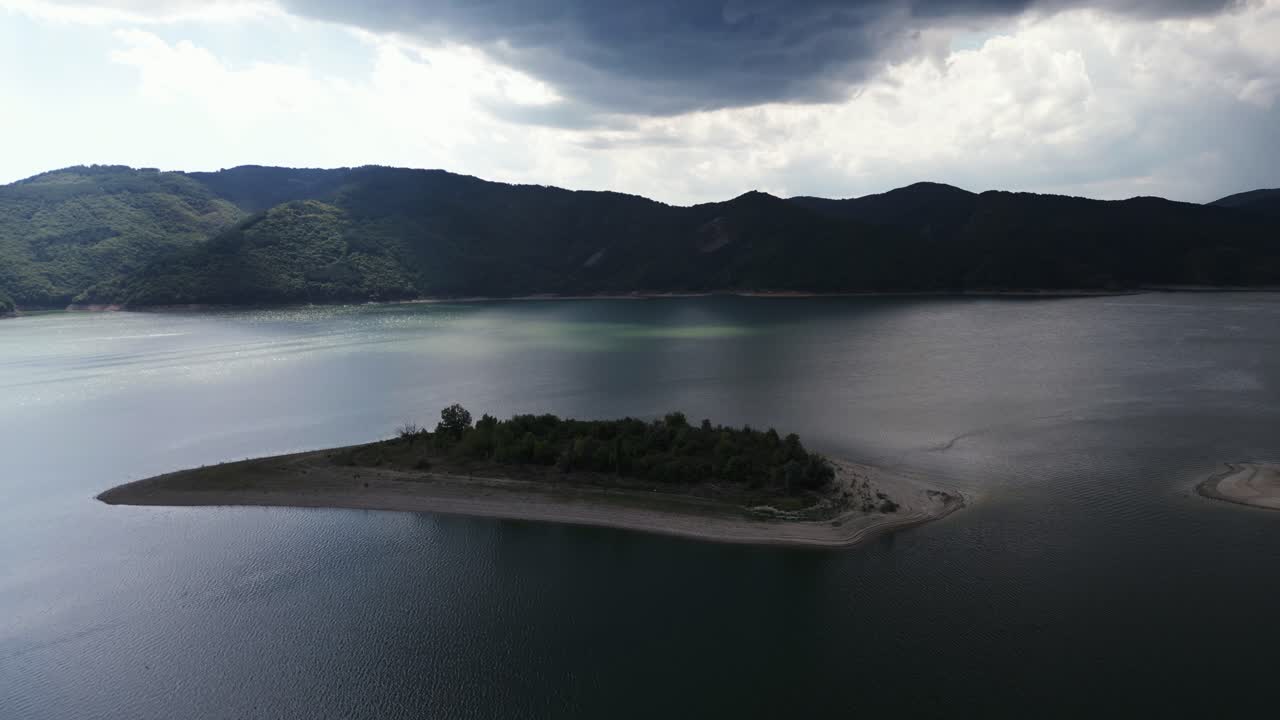 산악 지형 위에 어두운 폭풍 구름이 어있는 저수지 한가운데에 있는 섬의 극적인 공중 촬영