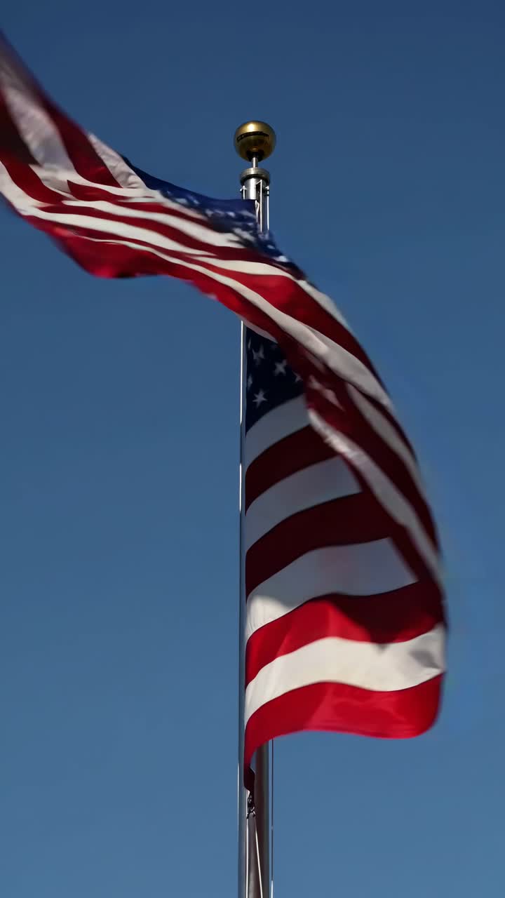 Ripresa video dal basso di una bandiera americana che sventola contro un cielo azzurro limpido, catturando il movimento.