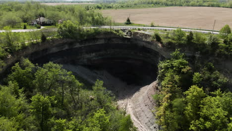 aerial backwards shot of famous devil's punch bowl surrounded by farm fields during summer in canada