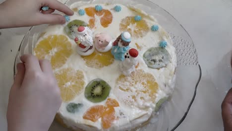 close-up, mom and daughter decorate christmas cake figures of santa claus and animals. cake with white cream and fruit is on a glass plate. the concept of preparing a family holiday. 4k.