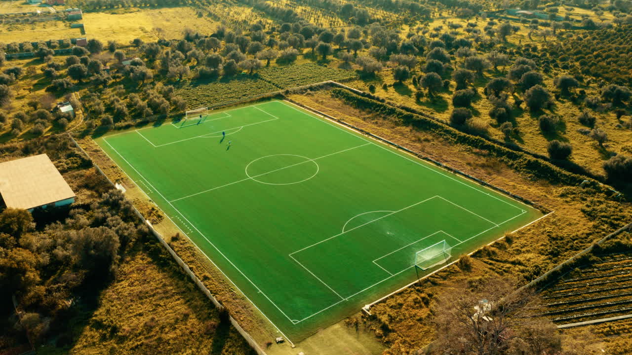 Campo de futebol verde na natureza entre oliveiras e árvores frutíferas.
