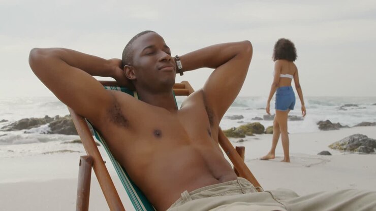 Vista frontale di uomo afroamericano che si rilassa con gli occhi chiusi sulla spiaggia 4k