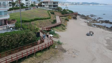 Aerial-landscapes-over-calm-beaches-at-sunset-with-people-walking-along-the-coastal-path-of-the-town-of-Cala-de-Mijas,-in-the-province-of-Malaga,-Spain