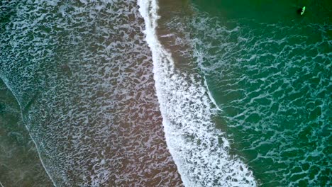 Aerial-shot-of-a-beach-at-night,-with-camera-moving-closer-to-crashing-waves-from-the-sea