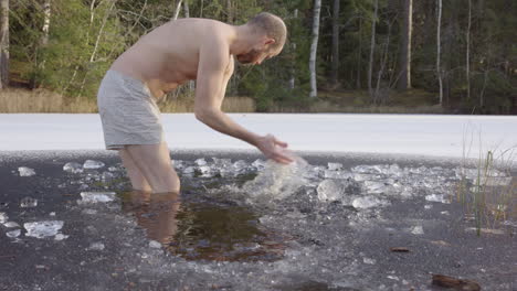 slow motion - a male ice bather clears ice from the bathing hole in the lake