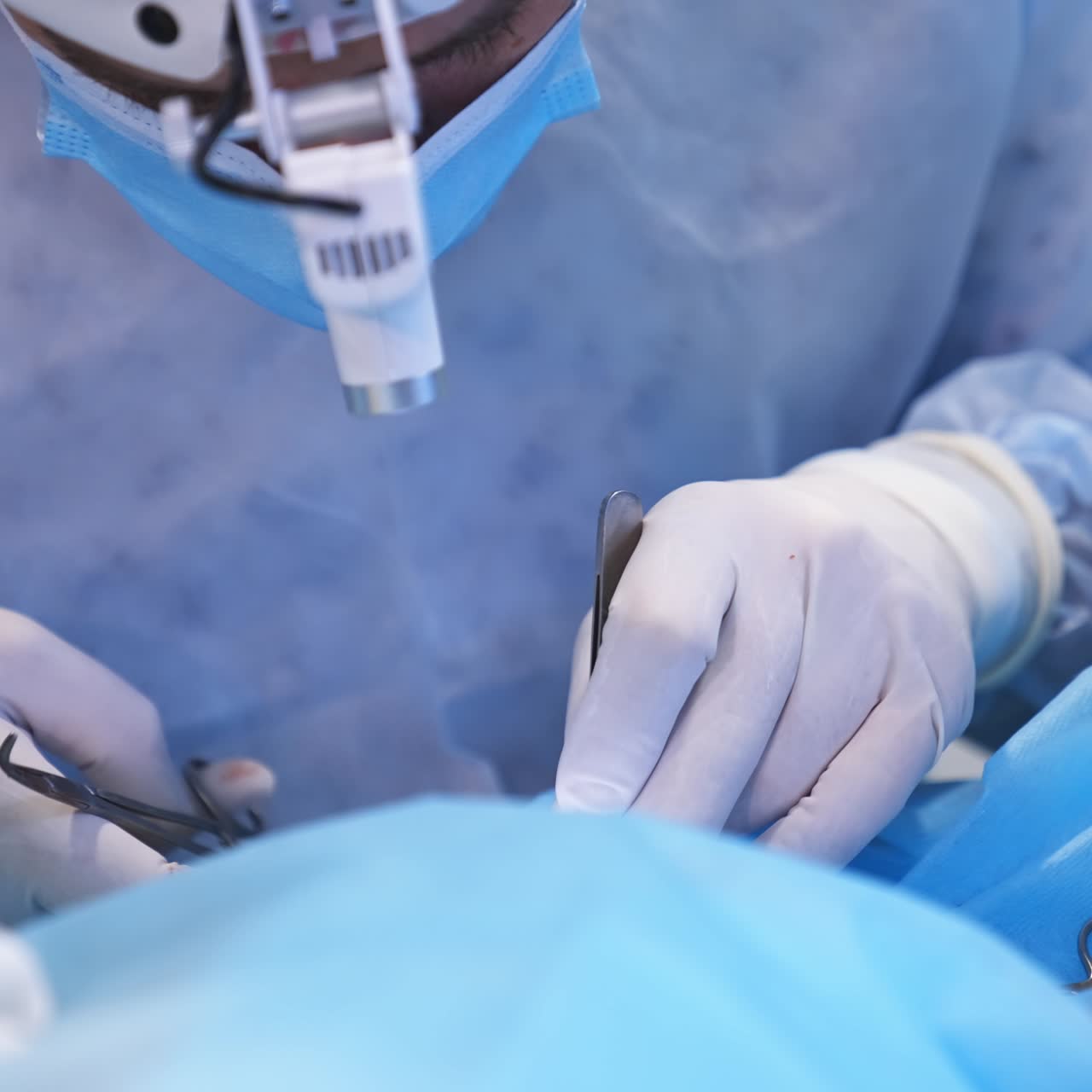 Surgeon's hands in latex gloves hold forceps ready to be used at operation. Doctors bend really low over the surgery locality. Close up
