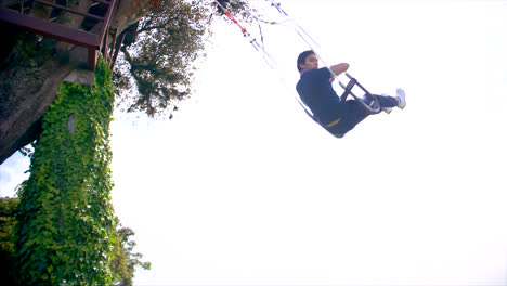 side slomo of young man going high on rope swing in nature in ecuador