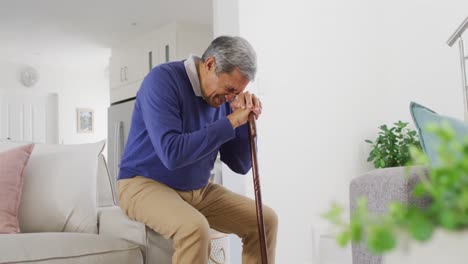 Video-of-tired,-sad-senior-biracial-man-sitting-and-leaning-head-on-walking-stick