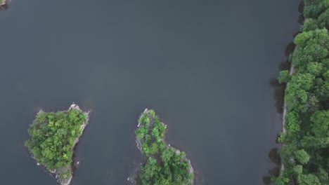 an aerial, top down view over calm waters with tiny islands with green trees on a cloudy day