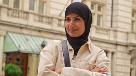 portrait of smiling muslim businesswoman wearing hijab and modern business suit standing and folding arms outside city office buildings 1