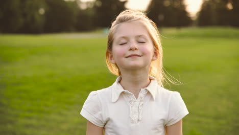 portrait of a cute blonde little girl with closed eyes smiling surronded by soap bubbles in the park