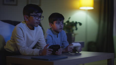 Dos-Niños-Pequeños-En-Casa-Jugando-Con-Una-Consola-De-Juegos-De-Computadora-En-La-Televisión-Sosteniendo-Controladores-A-Altas-Horas-De-La-Noche-7