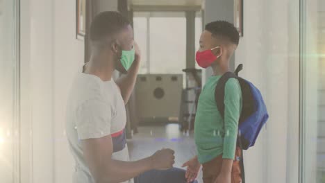 animation of lights over happy african american father and son in face masks and clapping hands