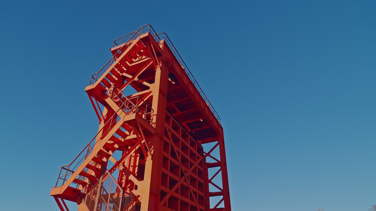 A dynamic low angle shot looking up at the Old Iwabuchi Sluice Gate. The bold red steel structure stands tall against a vibrant blue sky in Tokyo