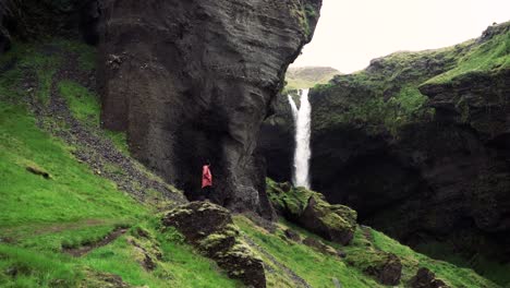 Tomas-En-Cámara-Lenta-De-Una-Remota-Cascada-Islandesa-Con-Un-Hombre-Caminando-Hacia-Ella