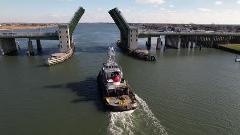 an aerial view behind a tugboat heading inland from the sea