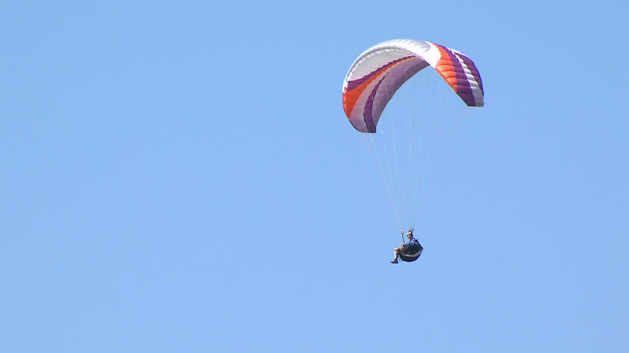 Paraglider with colorful parachute flies across blue sky on summer sunny day
