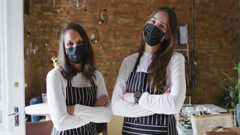 dos mujeres caucásicas con máscaras faciales y delantales, mirando a la cámara