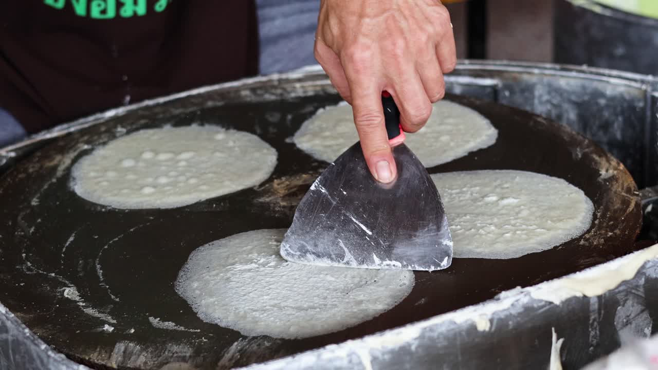 persona cocinando hábilmente panes planos en una parrilla grande
