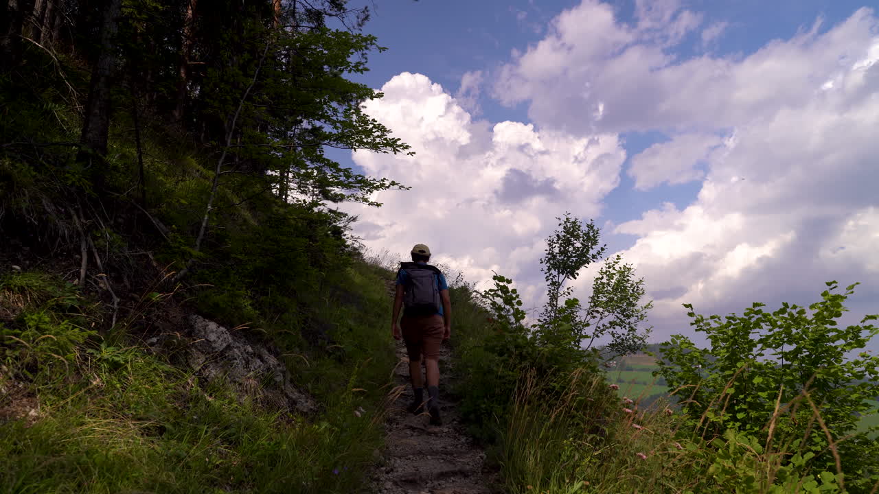 excursionista masculino caminando cuesta arriba con impresionantes formaciones de nubes en segundo plano.