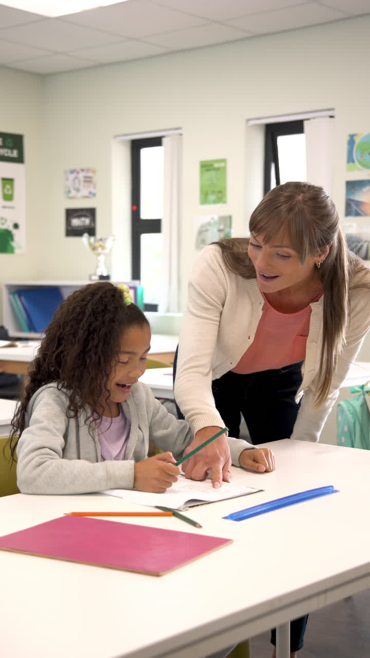 Vertical video: Teacher helping young student with homework in classroom, fostering learning
