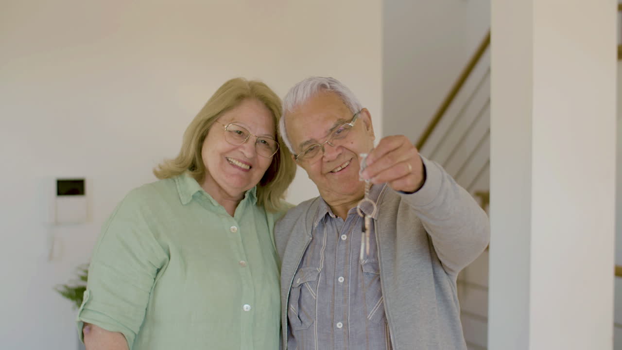 feliz pareja mayor mirando la cámara y mostrando las llaves de su nueva casa