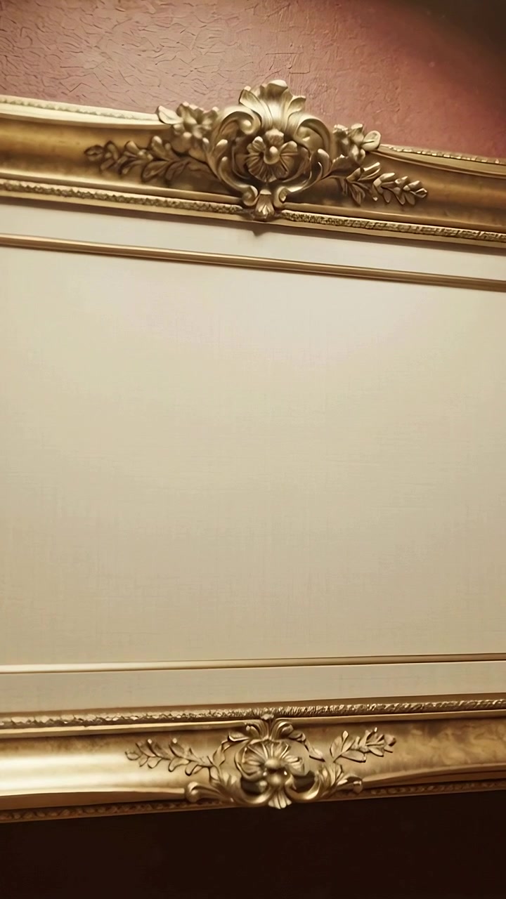 Video verticale: Telecamera che si inclina inquadrando un decoro dorato ornato con un pannello color crema su una parete bordeaux, centrando il motivo