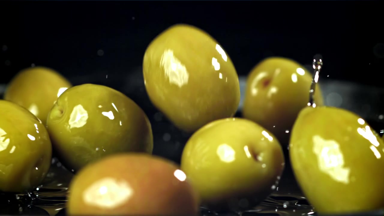 Olive verdi che cadono nell'acqua con schizzi al rallentatore