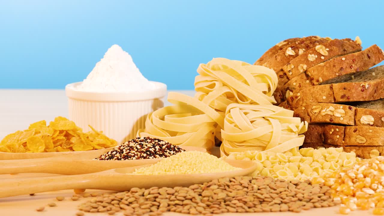 Various grains, pasta, and bread arranged on a wooden surface with a bright blue backdrop, highlighting texture and color
