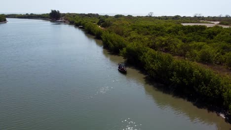 Canoe-Sails-with-Tourists-in-Summer-West-African-Destination,-River-Gambia,-Savanna-Landscape-aerial-shot